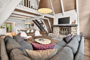A spacious living room with a high ceiling, a staircase, a fireplace, and a television mounted on the wall. - Adventure Awaits! Cozy Aframe 5 Min to Breck. (Breckenridge)