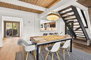 A spacious dining area with a high ceiling and a modern chandelier, leading to a kitchen and a staircase. - Adventure Awaits! Cozy Aframe 5 Min to Breck. (Breckenridge)