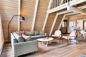 A loft-style living area with a high ceiling, wooden beams, a sofa set, a coffee table, and a dining table with chairs. - Adventure Awaits! Cozy Aframe 5 Min to Breck. (Breckenridge)