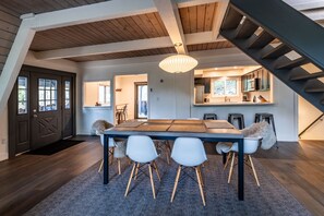 Un vaste espace de salle à manger avec une grande table et quatre chaises, un escalier et une cuisine en arrière-plan.