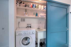 Uma lavanderia compacta com máquina de lavar, pia e prateleiras com produtos de limpeza.