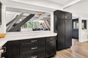 A modern kitchen with dark cabinetry, a white countertop, and a view of a living room through an open doorway. - Adventure Awaits! Cozy Aframe 5 Min to Breck. (Breckenridge)