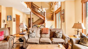 A spacious living room with a large leather sofa, a wooden staircase, and a dining area with a table and chairs.