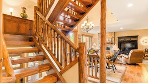 A wooden staircase with a chandelier, a dining area with a table and chairs, and a television in a living room.