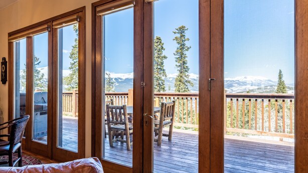 Ein Zimmer mit großen Schiebeglastüren, die auf eine Terrasse mit Sitzgelegenheiten und Bergblick führen.