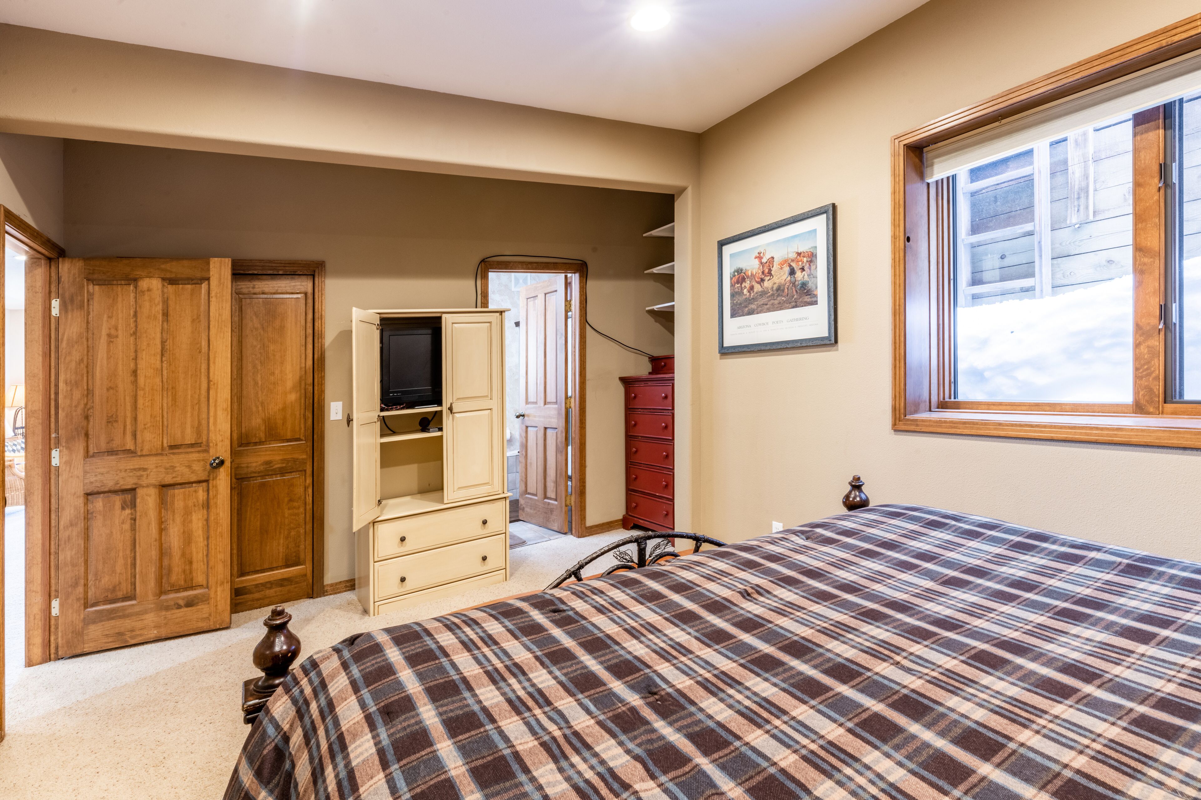 Une chambre à coucher avec un lit, une armoire en bois, une commode et une fenêtre donnant sur un beau paysage.
