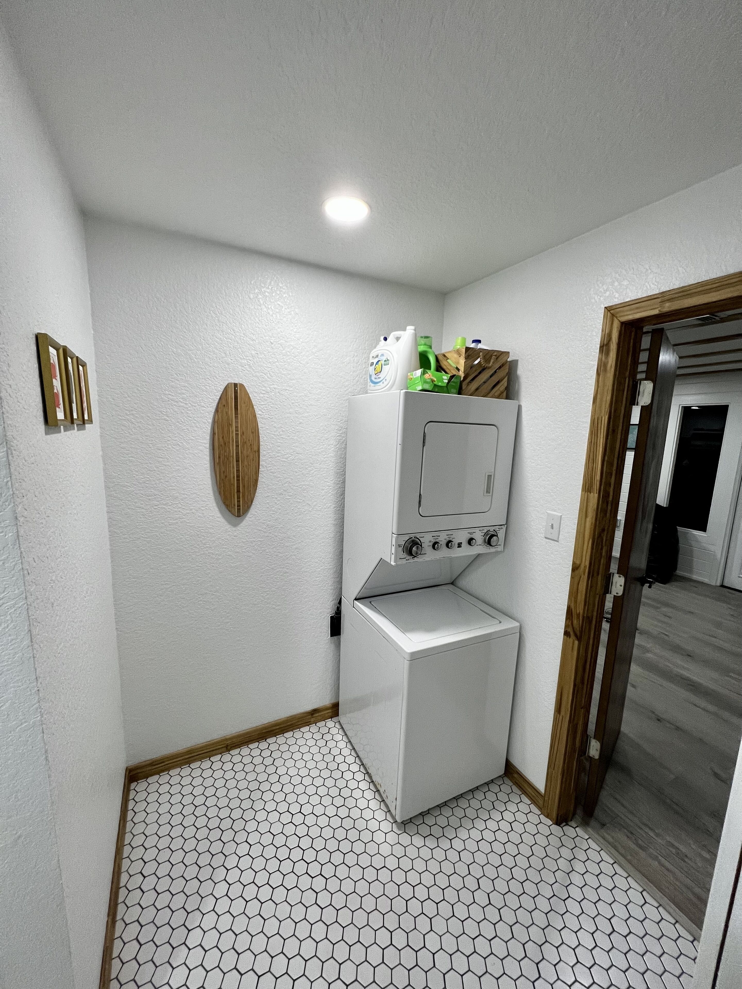 A compact laundry room with a washing machine and dryer, a wooden wall decoration, and a hexagonal tiled floor.