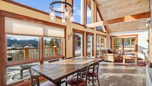 A spacious room with a large wooden table and chairs, large windows offering mountain views, and a cozy seating area with a sofa and coffee table.