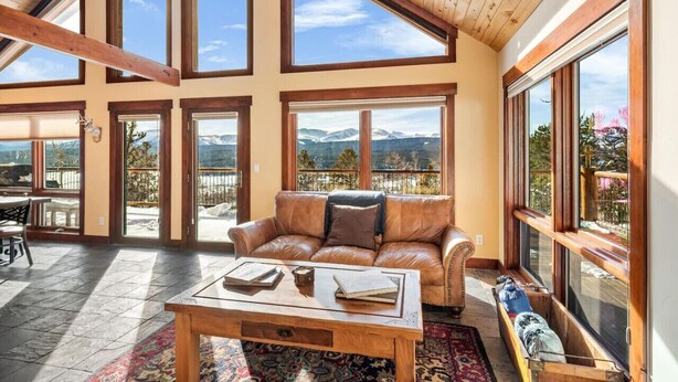 A spacious living room with a leather sofa, a wooden coffee table, and large windows offering mountain views.