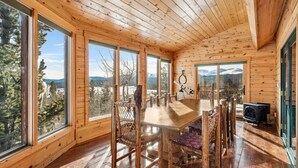 A wooden cabin with a dining area, large windows, and a view of mountains.