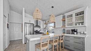 A modern kitchen with white cabinetry, a large island with bar stools, and pendant lighting. - Oceanfront 4BR | Porch Swinging + Dolphin Watching (Surf City)