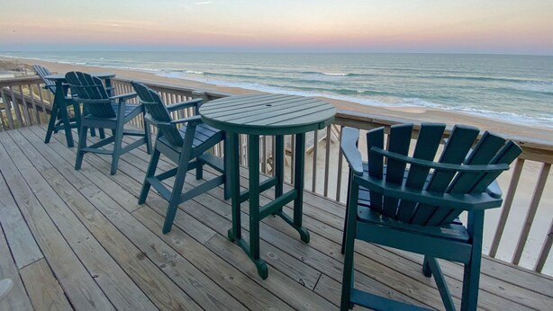 A wooden deck with green Adirondack chairs and a table overlooking the ocean. - Oceanfront 4BR | Porch Swinging + Dolphin Watching (Surf City)
