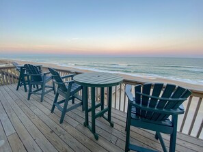 Une terrasse en bois avec des fauteuils Adirondack verts et une table donnant sur l’océan.