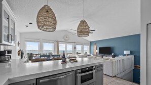 A modern kitchen with stainless steel appliances, a large island, and a dining area with a view. - Oceanfront 4BR | Porch Swinging + Dolphin Watching (Surf City)