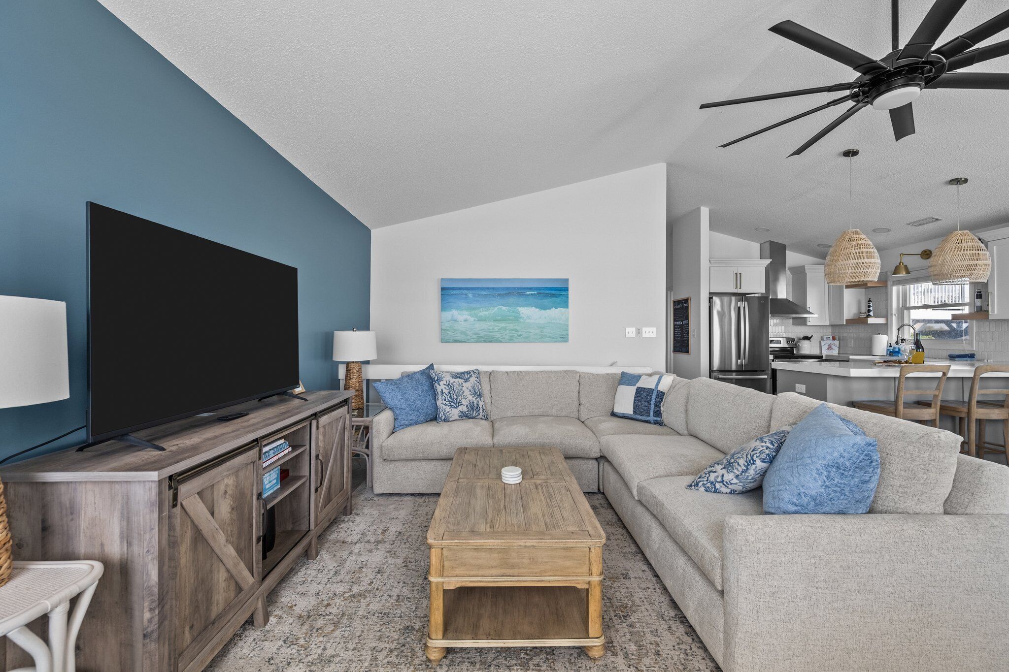 A living room with a sectional sofa, a wooden coffee table, a flat-screen TV, and a ceiling fan.