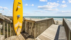 A wooden boardwalk leading to a beach with a yellow surfboard leaning against the railing. - Oceanfront 4BR | Porch Swinging + Dolphin Watching (Surf City)