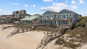 A beachfront property with multiple buildings, wooden walkways, and a sandy beach. - Oceanfront 4BR | Porch Swinging + Dolphin Watching (Surf City)
