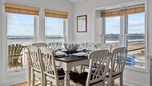 A dining area with a table set for four, large windows with ocean views, and a framed picture on the wall. - Oceanfront 4BR | Sandcastles + Golden Sunrises (Surf City)