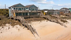 A beachfront property with multiple buildings, including a prominent two-story house with a balcony and a smaller structure nearby. - Oceanfront 4BR | Sandcastles + Golden Sunrises (Surf City)