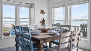 A dining room with a view of the beach, white walls, and a wooden table set for four. - Twin Landings | Two Homes, One Epic Family Escape! (Surf City)
