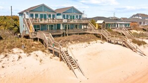 A beachfront property with a two-story building featuring a wooden deck and a staircase leading to the beach. - Twin Landings | Two Homes, One Epic Family Escape! (Surf City)