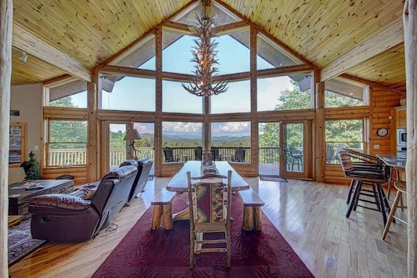 A spacious room with a large wooden ceiling, a dining table with chairs, a sofa, and a view of the outdoors.