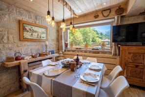 A dining area with a rustic stone wall, wooden ceiling, and a large window offering a view of trees and mountains. - Grangettes 1 ski-in & ski-out (Les Allues)