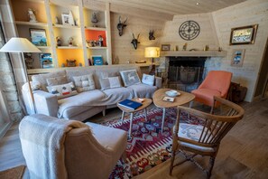 Un accogliente soggiorno con divano, poltrone, camino e libreria con oggetti decorativi.