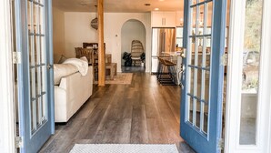 A home interior with a wooden floor, a sofa, a chair, and a kitchen area visible through an open door. - 30a Calm Gulf Cottage -1 mile from beach + golf cart (Santa Rosa Beach)
