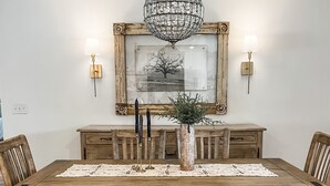 A dining room with a wooden table, benches, a chandelier, wall-mounted lamps, and a framed picture. - 30a Calm Gulf Cottage -1 mile from beach + golf cart (Santa Rosa Beach)
