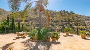 An outdoor patio with a table and chairs, surrounded by potted plants and a palm tree, overlooking a hilly landscape. - Casa La Mirada - RCP152 Cómpeta by Ruralidays (Málaga)