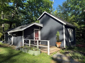A small, dark-colored cabin with a porch, a red door, and a potted plant. - Junebug Cottage: peace, love and privacy a short walk to Woodstock village green (Woodstock)