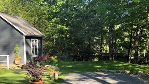 Une maison avec une allée en gravier, une terrasse en bois et un jardin agrémenté de plantes en pot.