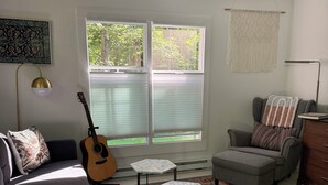 Un salon avec un canapé, une table basse, un tapis, une guitare et une fenêtre avec des stores.
