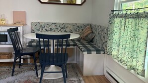 Une pièce comprenant une table ronde, des chaises, un banc, un miroir, une fenêtre avec des rideaux et un radiateur.