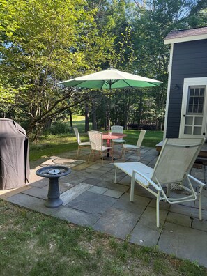A patio with a table, chairs, a covered grill, and a stone fountain. - Junebug Cottage: peace, love and privacy a short walk to Woodstock village green (Woodstock)