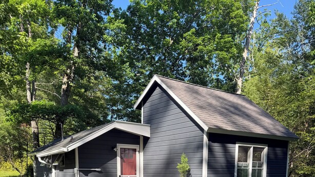 Une petite cabane avec une véranda, une porte d’entrée et une plante en pot.