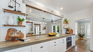 A kitchen with white cabinets, a wooden countertop, and a built-in oven. There are shelves with plants and decorative items, and a large window providing natural light. - 1910 Farmhouse: Chef’s Kitchen + Fire Pit + Studio - Near Wedding & Wine Country (Wilsonville)