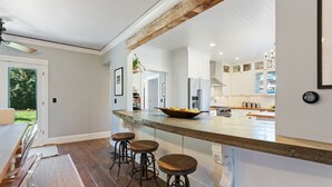 A modern kitchen with a large island, bar stools, and a view of the backyard. - 1910 Farmhouse: Chef’s Kitchen + Fire Pit + Studio - Near Wedding & Wine Country (Wilsonville)