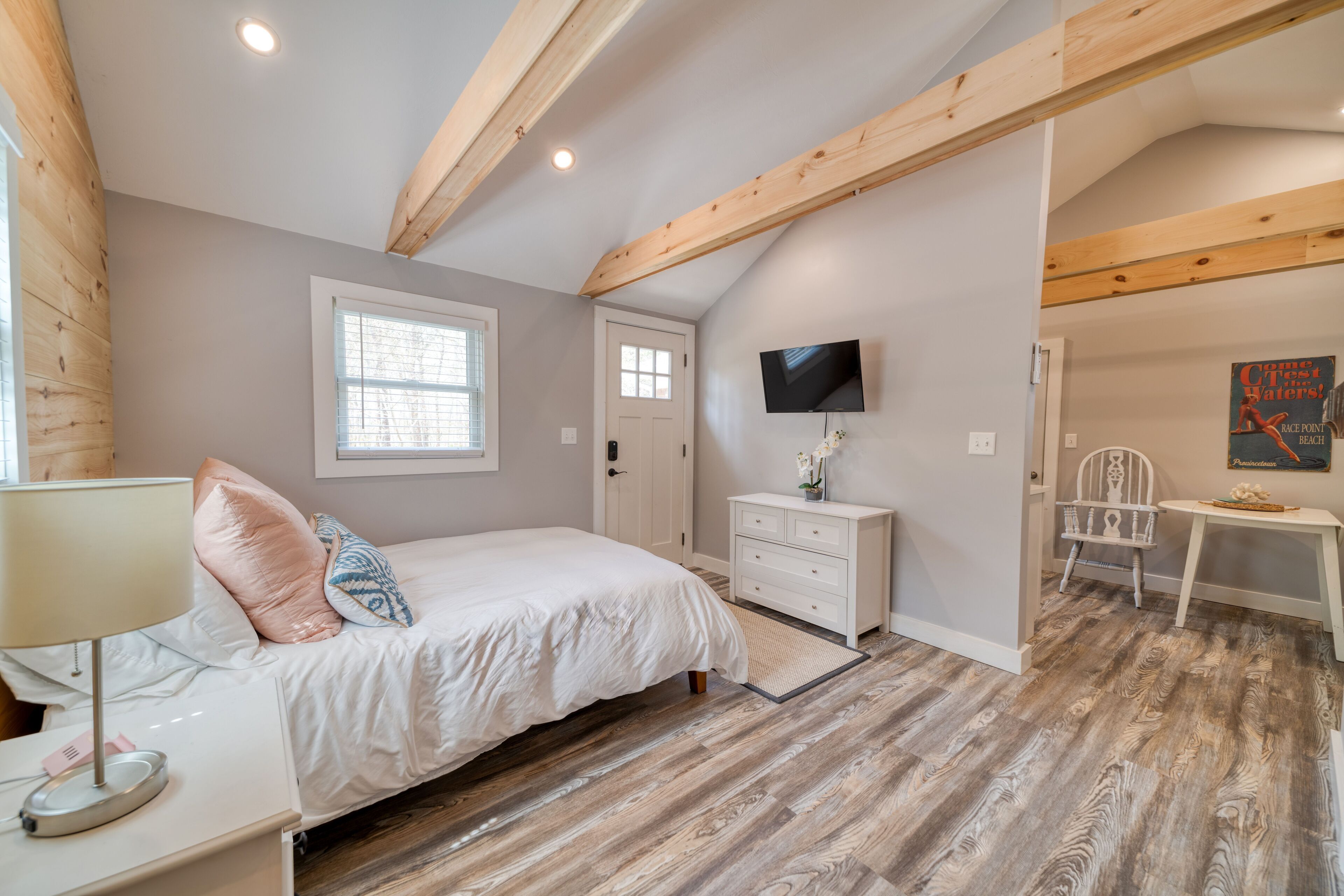 A bedroom with a bed, bedside table, dresser, TV, and a chair.