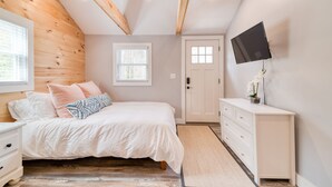Ein Schlafzimmer mit Bett, Kommode, Wandfernseher und Fenster.