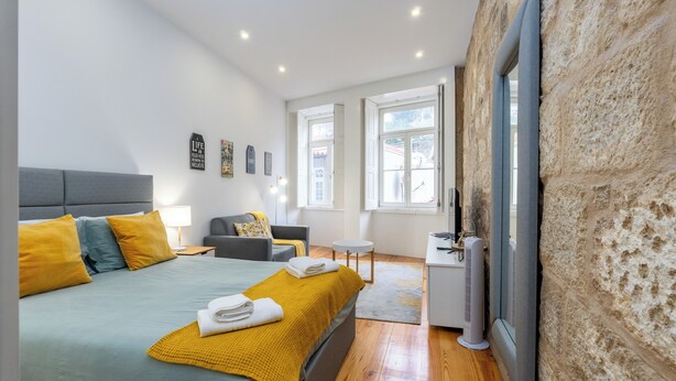 Un dormitorio moderno con una cama grande, mesitas de noche, un pequeño escritorio y una pared de piedra.
