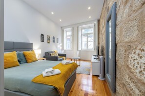 Un dormitorio moderno con una cama grande, mesitas de noche, un pequeño escritorio y una pared de piedra.
