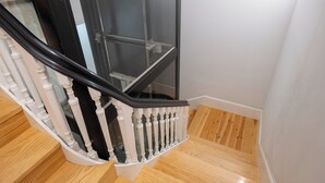 Una escalera con balaustres blancos y barandilla negra, que conduce a una habitación con piso de madera.