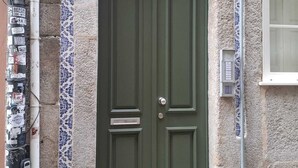 Una puerta verde con una placa con el número '83' encima, una pequeña ventana a la derecha y una pared con un estampado floral azul.