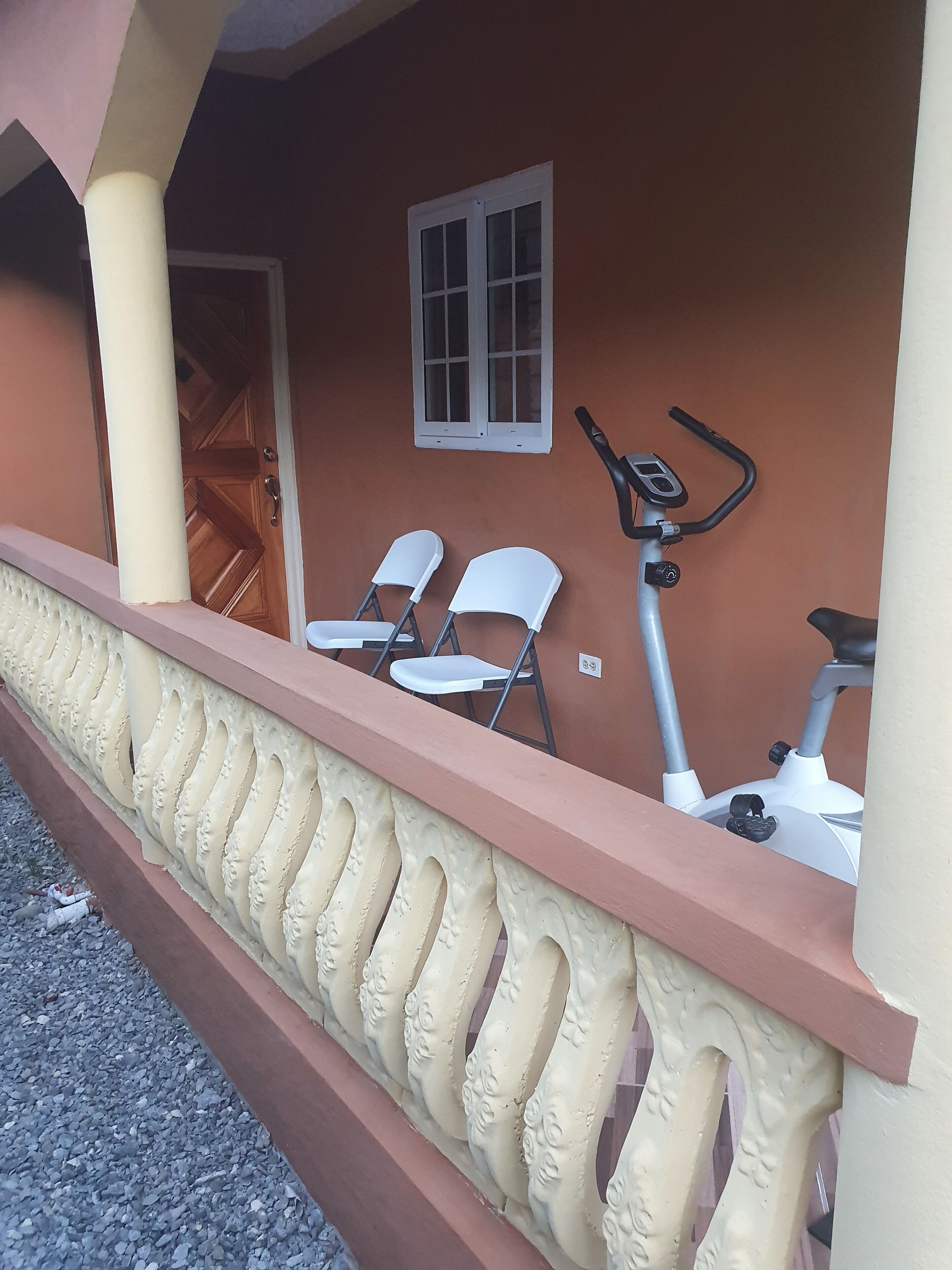 A balcony with a white railing, two white chairs, and an exercise bike.