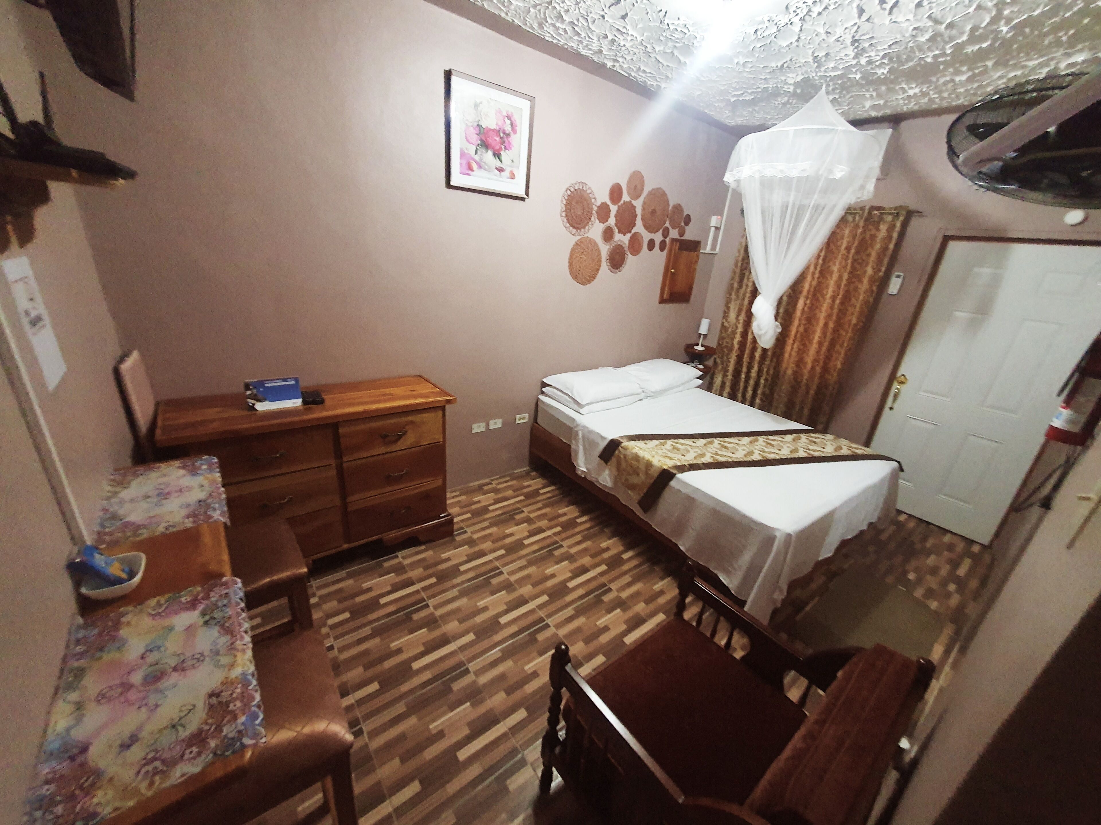 A small, neatly arranged bedroom with a bed, a wooden dresser, a desk, and a chair.