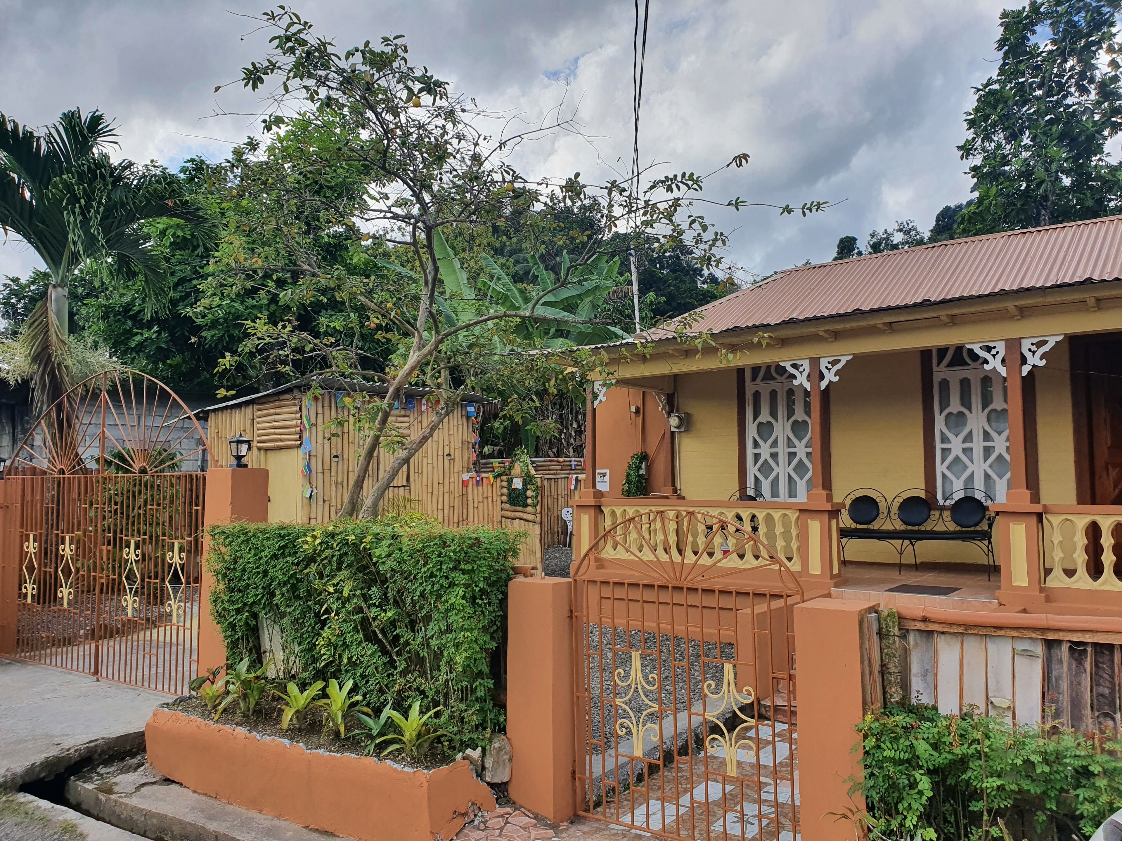 A house with a yellow facade, a gated entrance, and a small porch with decorative railings.