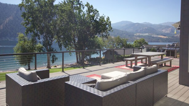 Una terrazza esterna con vista su un lago e montagne, con zona barbecue e posti a sedere all'aperto.