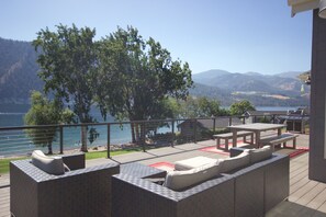 Een terras buiten met uitzicht op een meer en bergen, met een barbecuehoek en zitplaatsen.